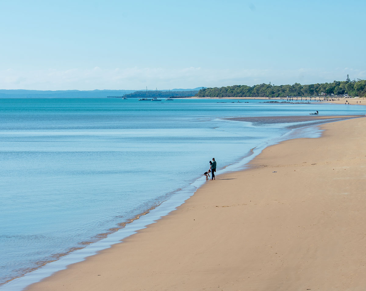 Sandy beach with calm blue water and people beside the shoreline