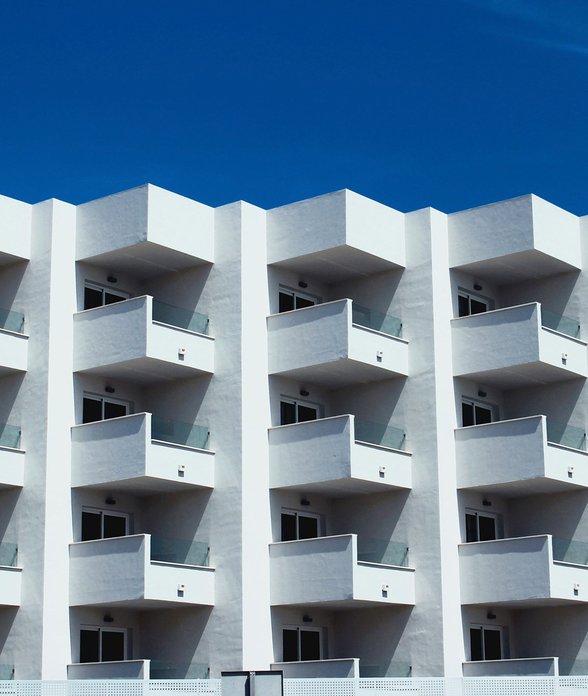 White apartment building with repeating balconies against a blue sky