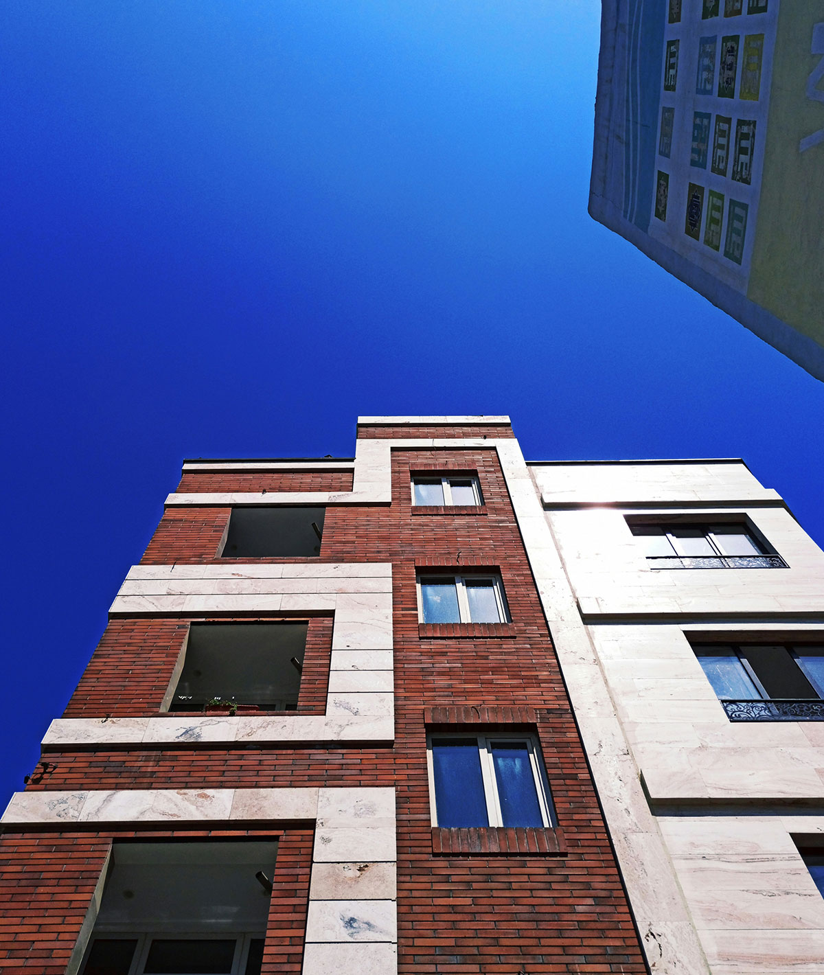Brick and cream apartment building viewed from below against a blue sky