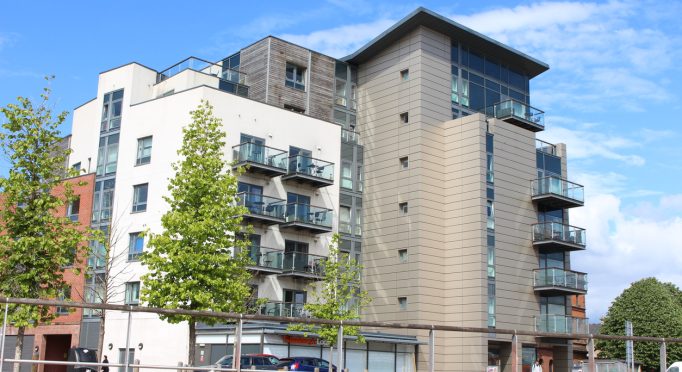 Cardiff Bay, Cardiff, United Kingdom - 10 May 2019:  A photograph of flats in Cardiff Bay, in bright sunlight.  Chairs on balconies, and trees around the apartment block.  Happy urban living concept. A Sainsbury's convenience store underneath the apartments