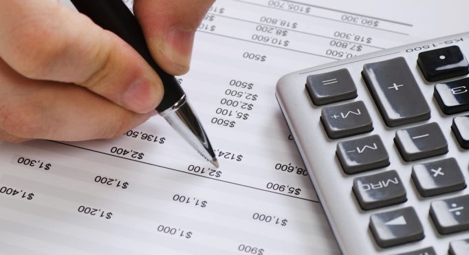 Financial data analyzing. Close-up photo of a businessman's hand counting on calculator in office. Selective focus